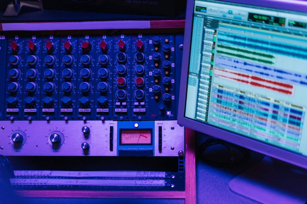 Close-up of a mixing console and screen in a recording studio, showcasing audio editing software.